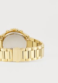 Goldfarbene Edelstahl-Uhr mit einem metallischen Armband, ausgestattet mit einem runden Gehäuse und mehreren Drückern an der Seite.