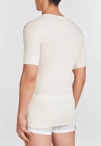 Maglietta a maniche corte, di colore crema a coste con scollatura rotonda. Presenta una forma aderente e una consistenza liscia, abbinata a pantaloni corti bianchi.