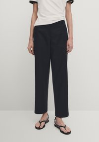 Niebieskie spodnie o szerokich nogawkach z lekkiego materiału o gładkiej fakturze, z bocznymi kieszeniami i dopasowanym krojem. W połączeniu z białą koszulą z czarnymi akcentami.