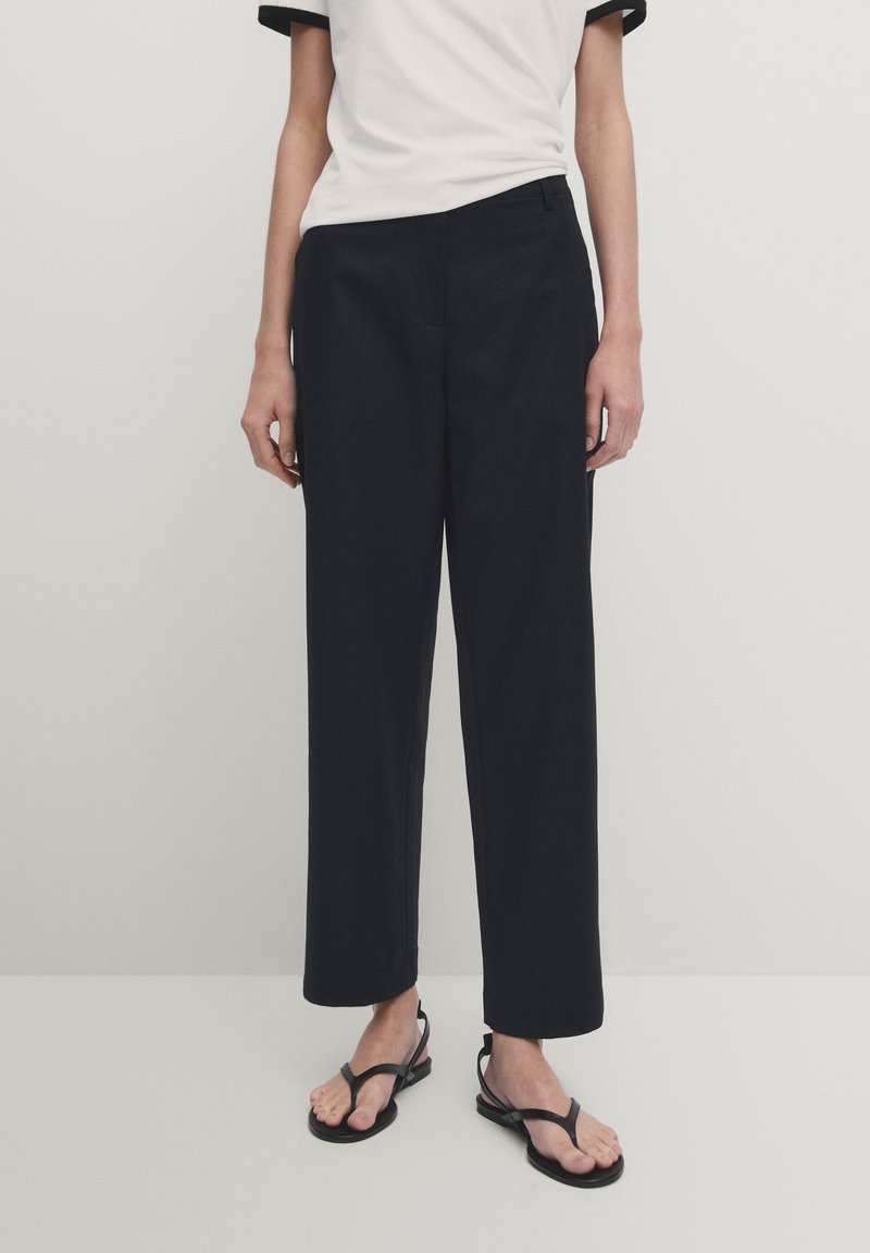 Niebieskie spodnie o szerokich nogawkach z lekkiego materiału o gładkiej fakturze, z bocznymi kieszeniami i dopasowanym krojem. W połączeniu z białą koszulą z czarnymi akcentami.