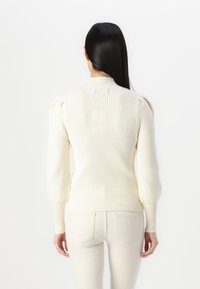 Pulover crem din tricot cu nervuri, guler înalt, mâneci tip balon și tiv ajustat. Proiectat cu un material texturat și un stil minimalist.