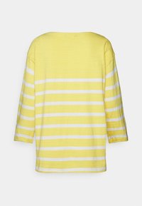 T-shirt amarela riscada com mangas de três quartos. Textura suave, com largas riscas brancas. Corte solto com decote redondo.