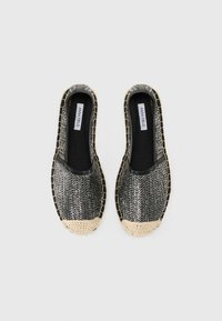 Sorte og sølvvevde slip-on sko med en strukturert overflate, lyst vevd tåhette og svarte gummidetaljer langs kantene.