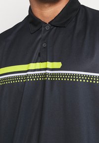 Mörkgrå pikétröja med en strukturerad ytfinish. Har ett grönt rand och en vit linje med prickiga accenter. Treknäppningsdesign.