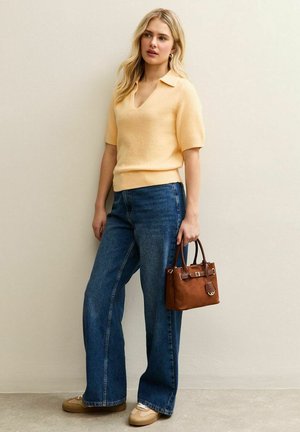 Pull à manches courtes jaune pâle, jean bleu à jambes larges et petit sac à main marron avec poignées supérieures. Chaussures décontractées de couleur claire.
