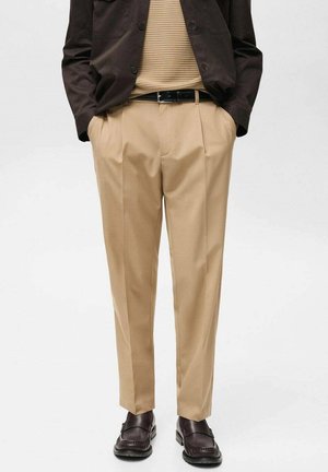 Beige tailored trousers with pleats, made from a smooth fabric. Features a relaxed fit and slight sheen. Paired with dark brown shoes.