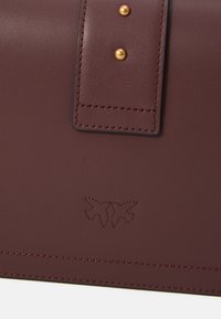 Maroon leather bag with a smooth texture, featuring a prominent stitched flap and two gold-tone studs. Embossed logo detail on the front.