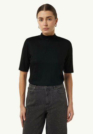 Schwarzer kurzärmeliger Rollkragenpullover, schmal geschnittenes Design, glatte Textur, kombiniert mit dunkelgrauen Jeans mit metallischen Nietenverzierungen.