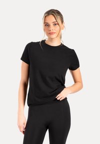 Camiseta negra de manga corta hecha de tela suave con cuello redondo y un ajuste relajado, combinada con leggings negros, sobre un fondo blanco.