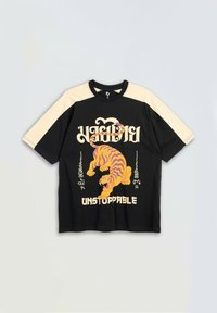 Czarna i beżowa koszula krótki rękaw z grafikom pomarańczowego tygrysa w pozycji roars oraz słowem "NIEZATRZYMANY" napisanym dużymi białymi literami.
