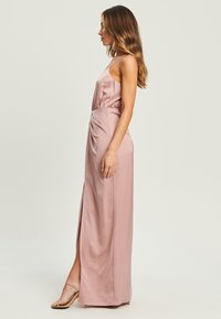 Long pink satin dress with a fitted waist, thin straps, and a thigh-high slit on one side. Smooth texture with a subtle sheen.