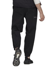 Svarta joggerbyxor i lätt tyg med elastiska avslut, försedda med en sidoficka och en minimalistisk vit tryckdetalj.