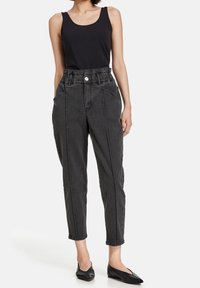 Top de tirantes negro combinado con pantalones de mezclilla de tiro alto en gris oscuro, con bolsillos laterales y cierre de botón, usados con zapatos planos negros.