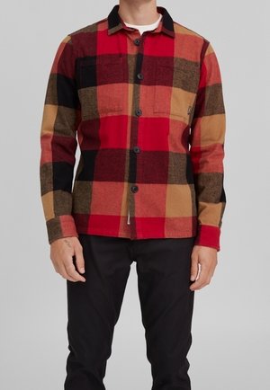 Röd, svart och brun rutig flanellskjorta med knäppning, två bröstfickor och kontrasterande svart krage. Mjuk textur.