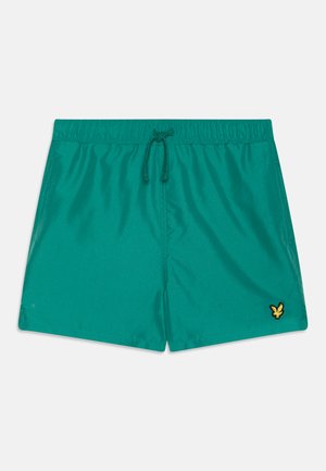 Shorts de bain turquoise en tissu lisse, avec une taille élastique dotée d'un cordon de serrage et un petit logo jaune sur le bas à gauche.