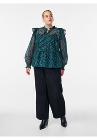 Teal Bluse mit Punkten, durchsichtigen Rüschensäumen, Peplum-Taille und Schlüssel-Ausschnitt; kombiniert mit dunklen, weiten Hosen und Knöchelstiefeln.