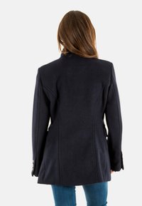 Trench coat in lana navy con una forma aderente, cuciture sulle spalle e polsini con bottoni; texture liscia, lunghezza media, design aderente sul retro.