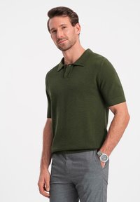 Mörkgrön kortärmad polo med en strukturerad väv, med en treknappslå och en klassisk krage. Matcher med grå byxor.