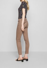 Getailleerde bloementop met korte mouwen, gecombineerd met getailleerde bruine broek. Dunne bandjes op zwarte hoge hakken, gladde stoftextuur.