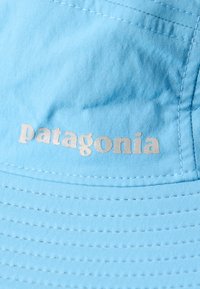 Ανοιχτό μπλε ύφασμα με ορατές ραφές και λογότυπο «patagonia» τυπωμένο με αντανακλαστικά ασημί γράμματα.