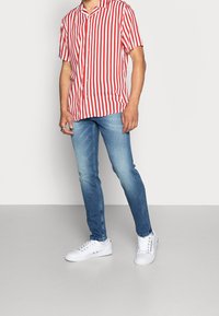 Camiseta de manga corta con rayas rojas y blancas, combinada con jeans ajustados azul claro y zapatillas blancas. Tela suave y ajuste informal.