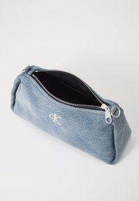 Denim lynlåspung med sølvhardware, der har en flad rektangulær form, subtil tekstur og indvendig i sort. Broderet logo på siden.