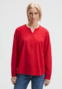 Rotes Langarmshirt mit V-Ausschnitt und Knopfleiste. Aus strukturiertem Stoff gefertigt, bietet es eine lockere Passform und hochgerollte Ärmel.