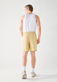 Lys beige shorts med elastisk talje og to baglommer. Sammen med en hvid ærmeløs skjorte og grå sneakers med gule accenter.