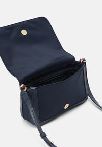 Bolso de mano azul marino con un acabado suave, cierre de broche dorado y correa ajustable. El interior incluye bolsillos y una sección con cremallera.