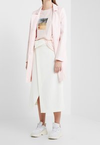 Vaaleanpunainen bleiseri graafisen t-paidan päällä, jossa on autiomaisema. Yhdistetty valkoiseen kietaisuhameeseen ja paksuihin valkoisiin lenkkareihin.