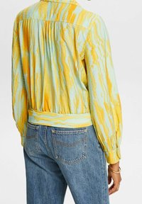 Blouse multicolore avec un motif ondulé bleu et jaune, tissu léger, manches longues, taille élastique et col à revers.