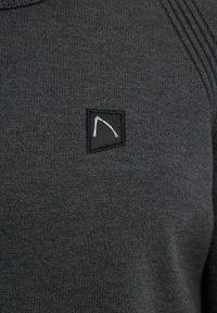 Donkergrijze geribbelde gebreide stof met een kleine zwarte vierkante patch, waarop een witte abstracte lijntekening is gestikt op het bovenste deel van de borst.
