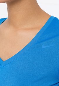 Camiseta azul de cuello en v hecha de tela suave, con un sutil logo de Nike en la parte superior izquierda, mangas cortas y un corte holgado.