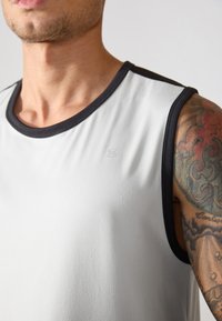 Graues ärmelloses Shirt mit schwarzem Saum, aus glattem Stoff gefertigt. Verfügt über ein dezentes Logo auf der Vorderseite und ein eng anliegendes Halsausschnitt-Design.