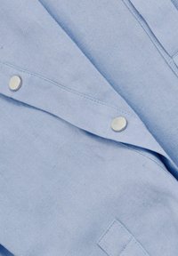 Camisa azul claro con una textura suave, que presenta botones a presión plateados y un cuello doblado. El material parece suave y casual.