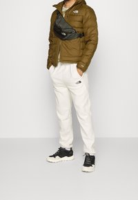 Olive puffer jacket, black fanny pack, cream sweatpants, and black athletic shoes with beige accents. Features logo branding on pants.