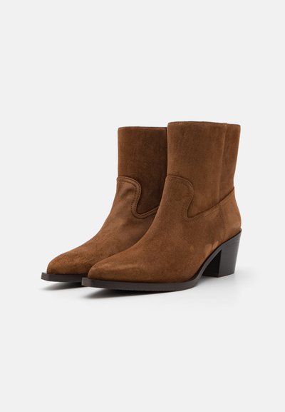 Bottines en daim marron avec un bout pointu et une tige courte, dotées d'un talon empilé et de détails cousus sur les côtés.