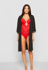 Juodas kimono stiliaus chalatas su nėrinių apdaila, dėvimas ant raudonos nėrinių bodysuit su gėlių raštu ir raktų skylute krūtinėje.