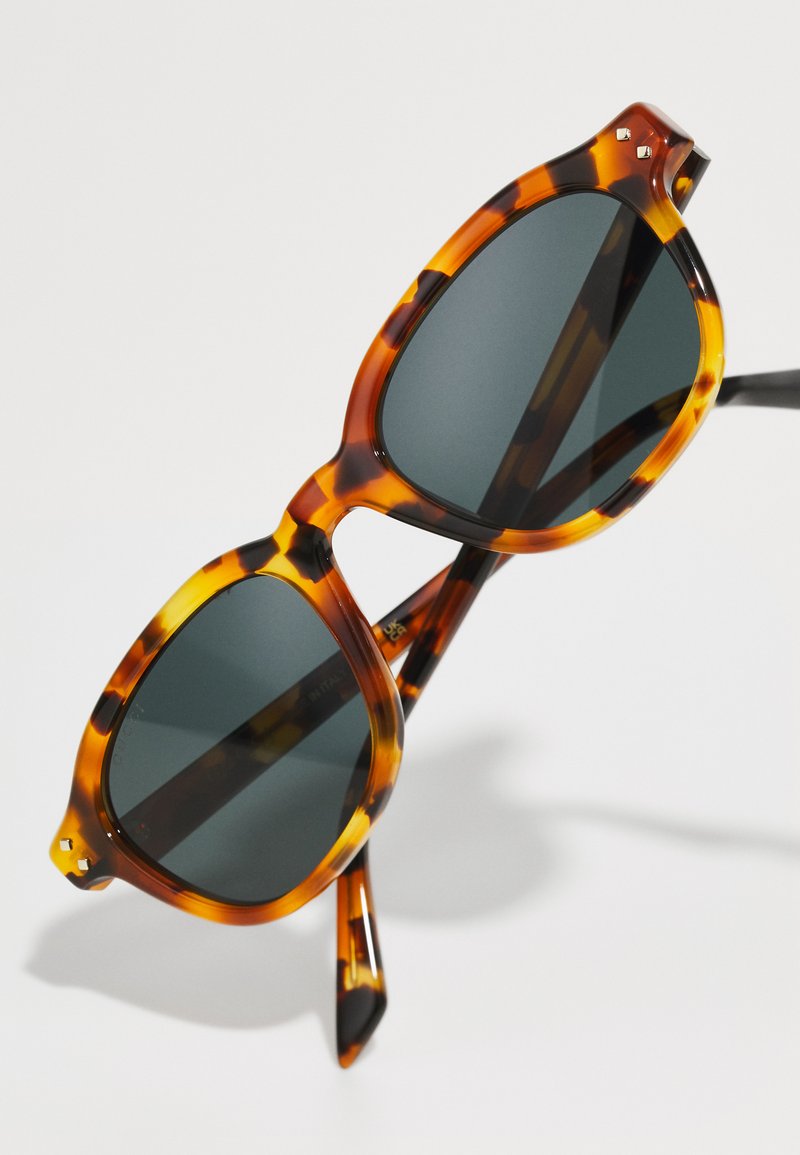 schildpad zonnebril met donkere glazen. Het montuur heeft een opvallend patroon en is licht oversized met taps toelopende pootjes en metal accents.