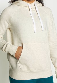 Hoodie color crema realizzato in morbido tessuto testurizzato. Presenta una tasca a marsupio, stringhe bianche e polsini e orli a coste.