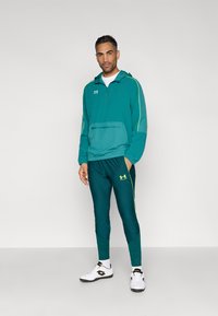 Τζελ αθλητικό μπουφάν με ημίκλειστο φερμουάρ και τσέπη μπροστά, σετ με αντίστοιχο κωνικό παντελόνι, με κίτρινες λεπτομέρειες και λογότυπα, φορεμένο με λευκά παπούτσια.