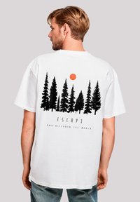 White t-shirt featuring a black forest silhouette and an orange sun graphic. Text below reads "ESCAPE AND DISCOVER THE WORLD."