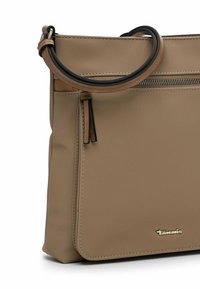 Beige synthetic handbag with a smooth texture, elongated shape, a top zip closure, and a contrasting brown leather handle and accents.