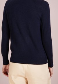 Mörkblå kashmirtröja med ribbad mudd och nederkant, med rundad halsringning och en mjuk textur, visad från baksidan.