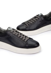Zapatillas de piel negra con cordones grises, que presentan una mediasuela blanca y un detalle del logo en la lengüeta, con textura suave y diseño casual.
