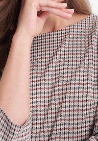 Mönstrad tyg med en strukturerad ljus färg som har små houndsse tooth-motiv i mörkbrun och svart. Bred halsringning och lös passform.