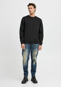 Zwarte sweater met ronde hals en lange mouwen, gecombineerd met blauwe jeans met vervaagde accenten, en zwarte chunky veterschoenen.