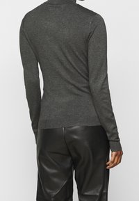 Czarnoszary sweter z długim rękawem, o wysokim dekolcie, z prążkowanymi mankietami i dopasowanym kroju, w połączeniu z czarnymi skórzanymi spodniami.