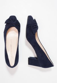 Décolleté in suede blu navy con punta tonda e dettaglio a fiocco annodato sul davanti. Tacco basso a blocco, interno liscio e suola nera.