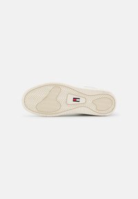 Talpa de sneaker albă cu cauciuc texturat, având un model în țesătură de hering. Un logo mic în roșu, alb și albastru este vizibil pe lateral.